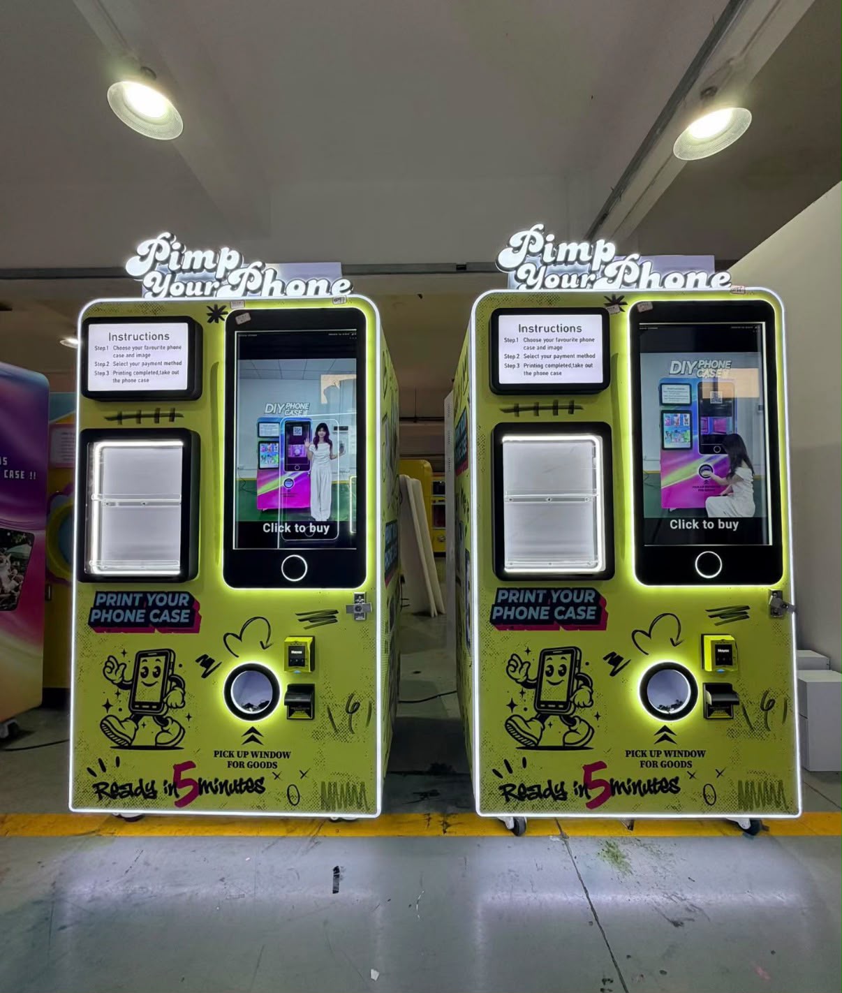 Two bright yellow-green Pimp Your Phone DIY phone case vending machines side by side, featuring cartoon mascot graphics.